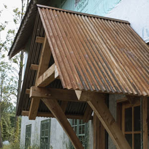 Side profile of a steeply pitched roof made of weathered, rusty corrugated metal panels on a timber frame
