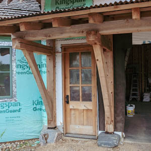 Close-up of a hand-cut timber frame post anchored to a large natural stone base with traditional joinery.