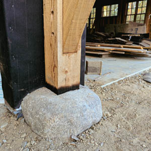 Close-up of an 8x8 Western Red Cedar post hand-scribed to fit a natural rock foundation footing.