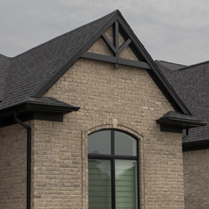 Timber framed gable truss painted dark grey on the front of a light colored brick home.